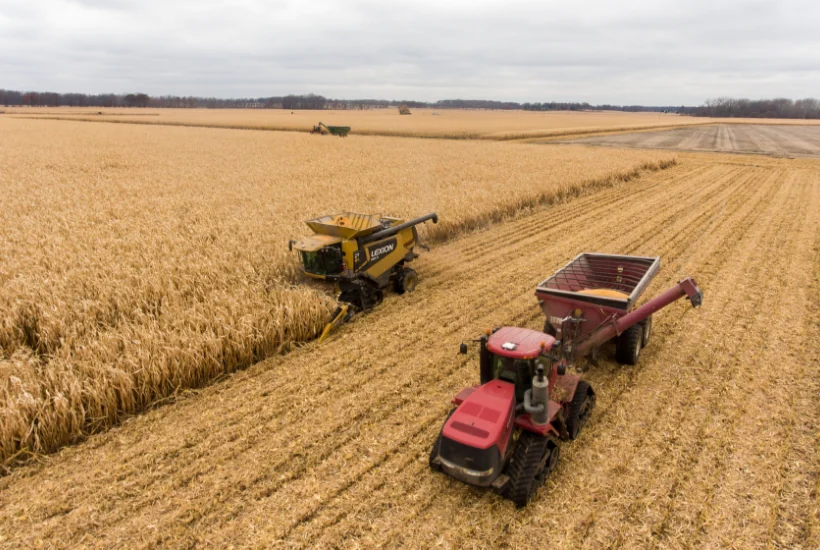 Harvesting equipment in a golden field, featuring a yellow combine harvester and a red tractor with a grain cart, under a cloudy sky, illustrating agricultural practices related to cryptocurrency discussions.
