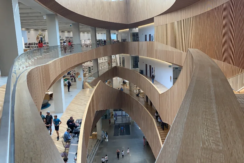 Modern architectural interior of a library featuring wooden spiral staircases, open spaces, and people engaging with the environment.