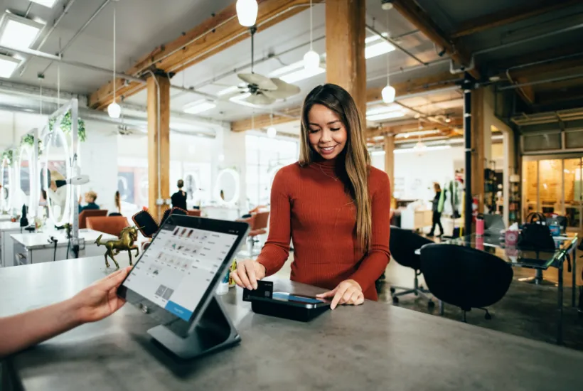 Woman making a payment at a modern retail counter, with a tablet displaying product options and a stylish interior setting.